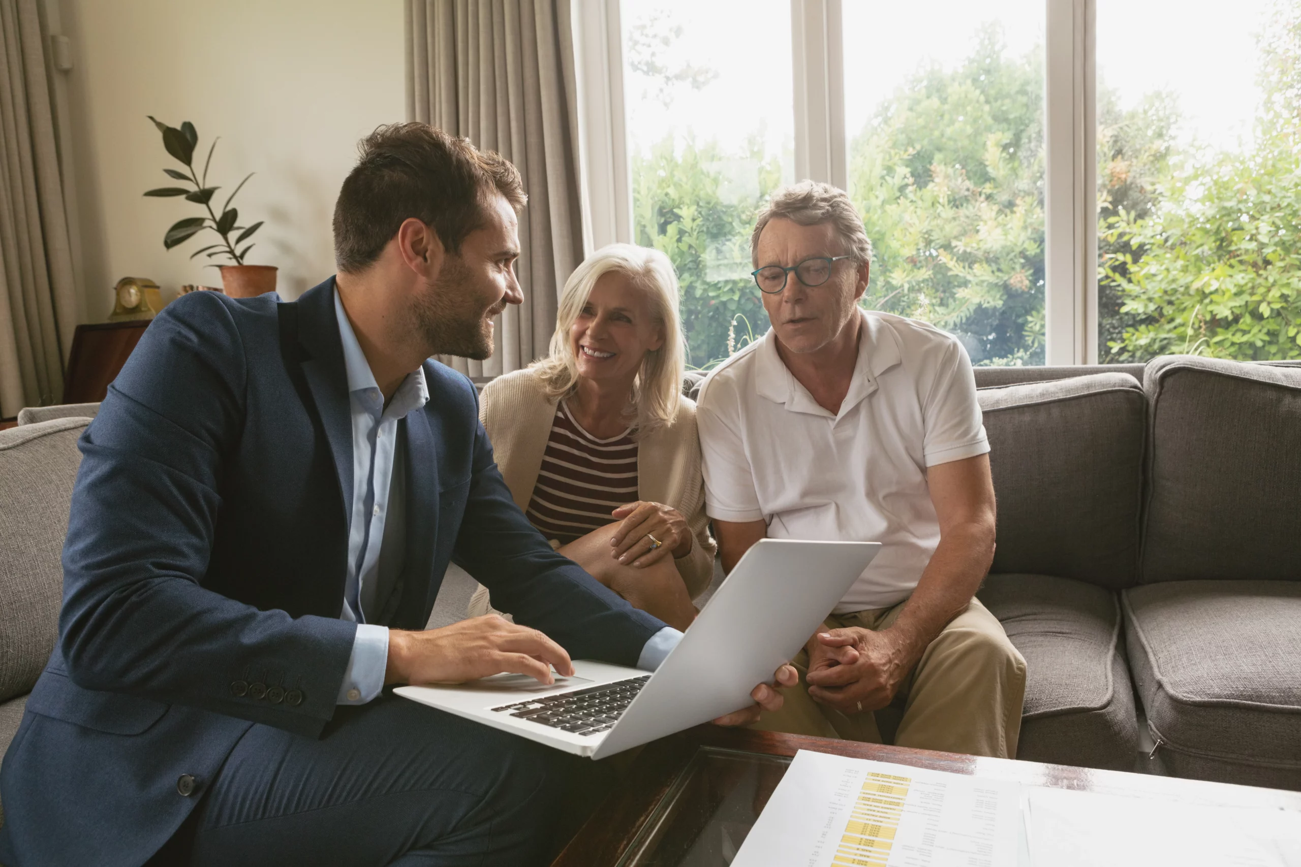 Businessman advising elderly couple via laptop in a living room setting, discussing estate plan protection