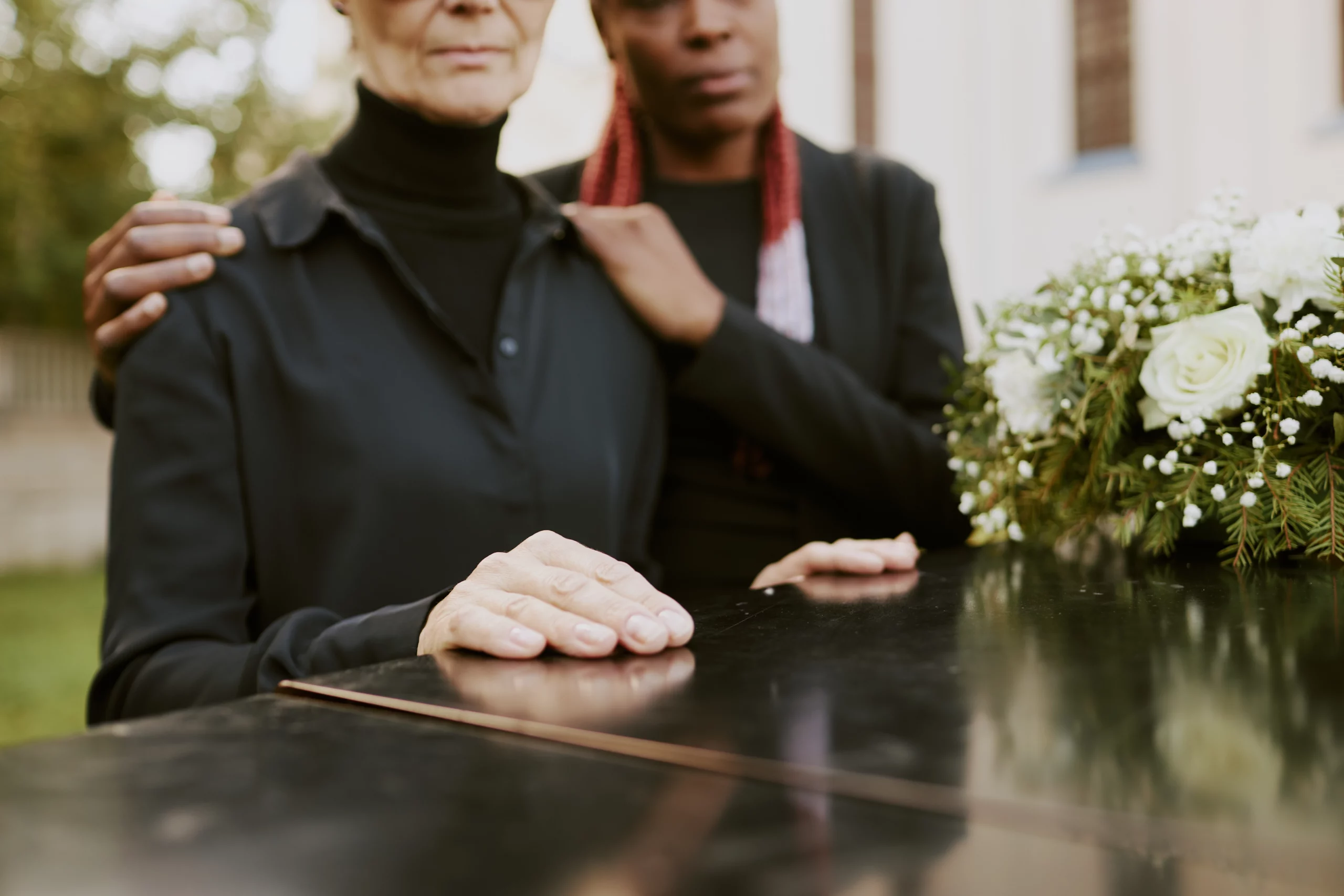 Two mourners in black at a funeral, one gently supporting the other — a visual representation of the emotional and legal uncertainty families face when someone dies without a will in California.