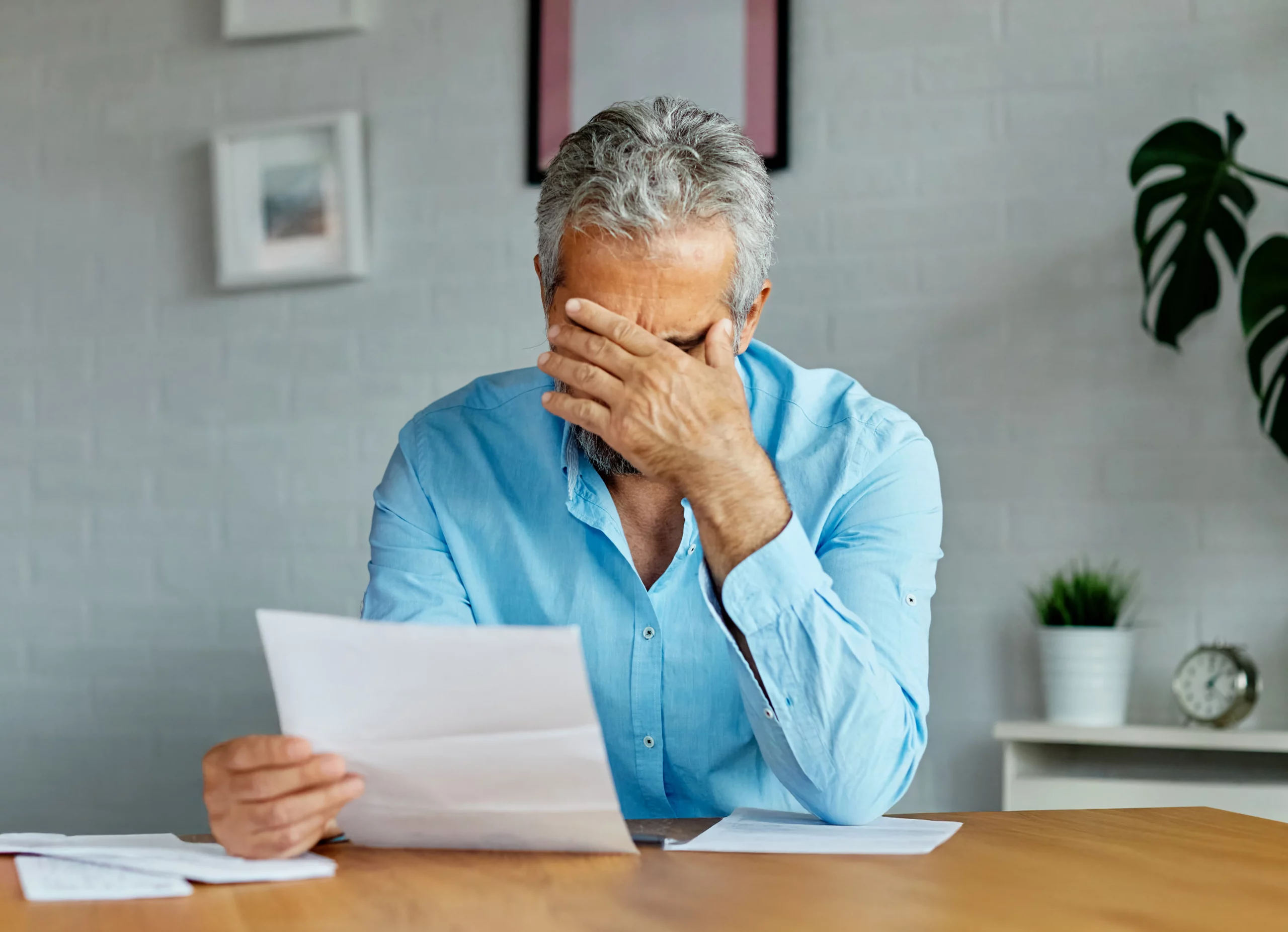 Stressed man in blue shirt at a table holding paperwork, illustrating frustration and concern in a San Diego beneficiary vs. trustee trust dispute.
