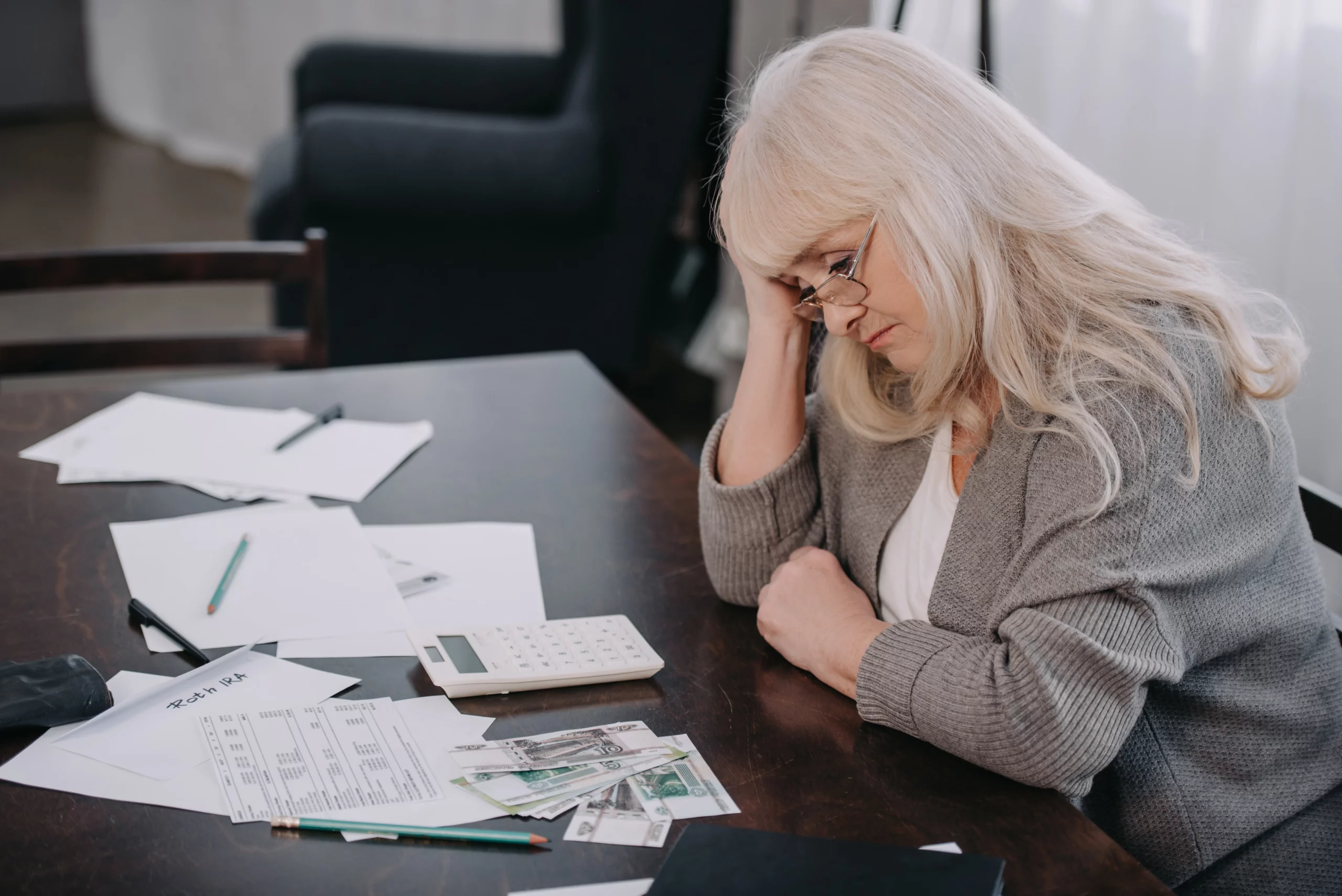 Elderly woman stressed at a table of papers, calculator, and cash, illustrating frustration over a trustee refusing to distribute trust assets in California.