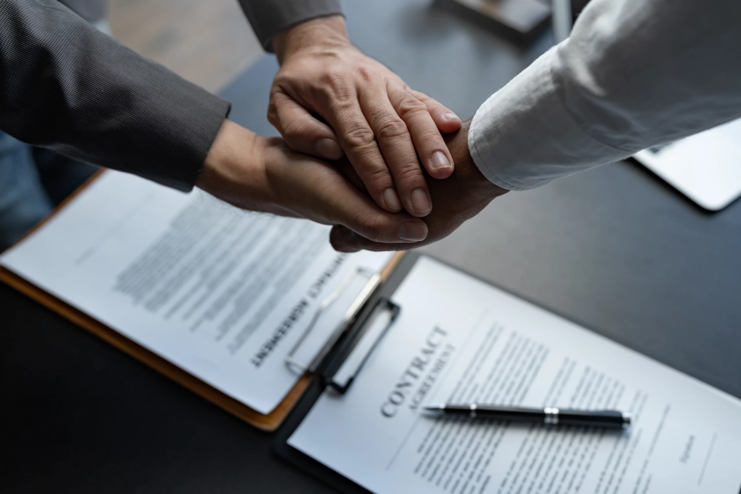 Two people shaking hands over signed contracts and pen on desk, illustrating beneficiaries agreeing to modify or terminate a trust under California trust law.