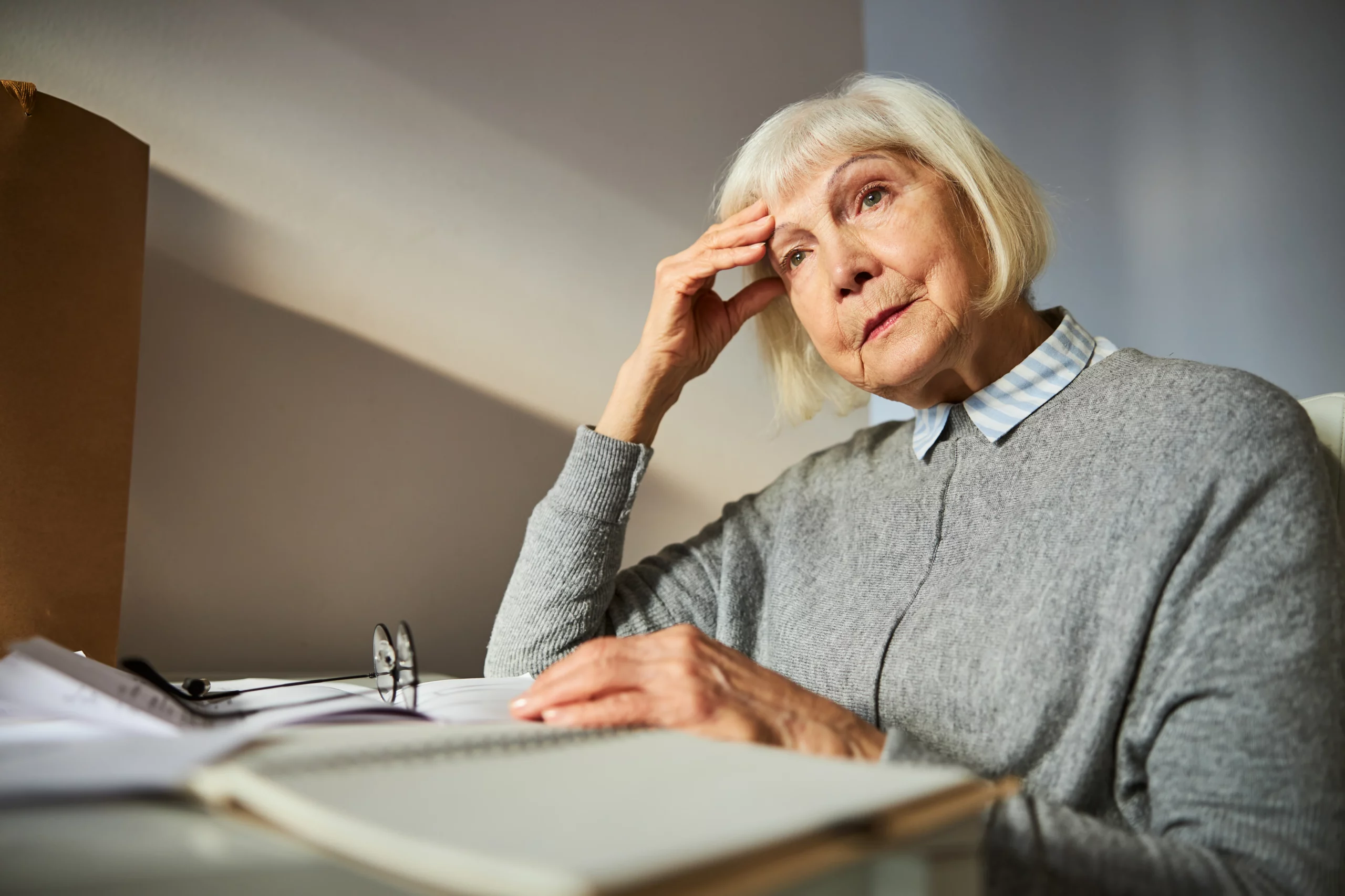 Elderly woman in gray sweater at a desk with papers and glasses, looking thoughtful about contesting a will after probate closed in California.
