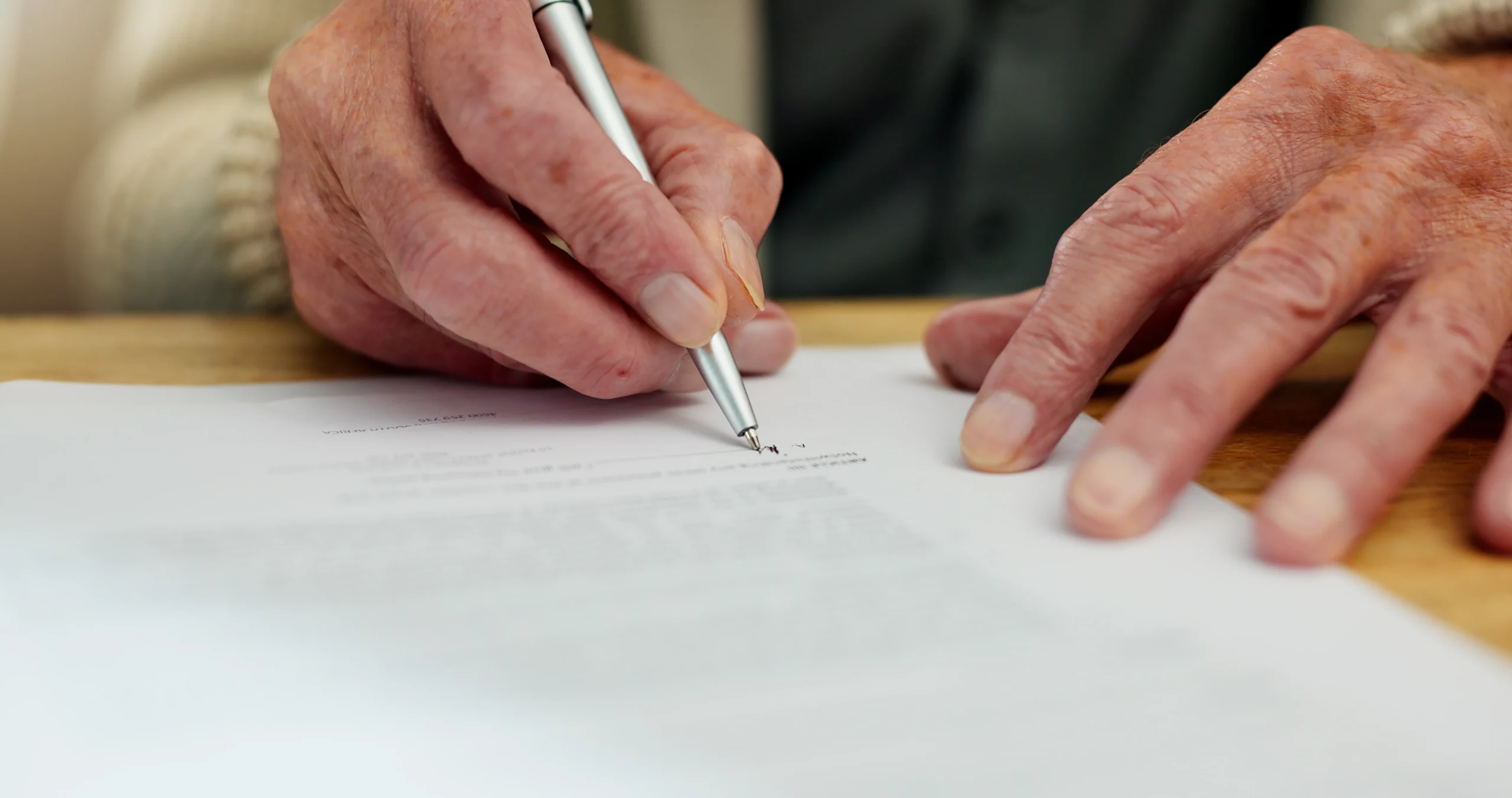 Elderly hands signing an important document on a wooden table, illustrating the careful legal process of removing an executor in California.