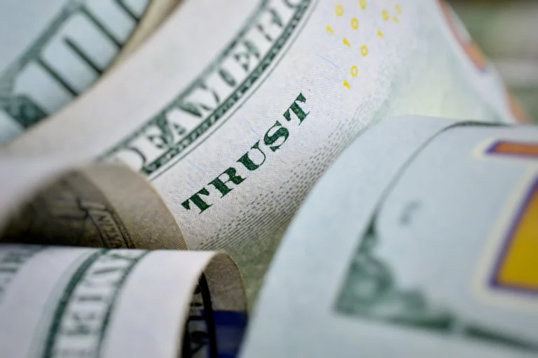 Close-up of a rolled US hundred-dollar bill showing the word ‘TRUST,’ symbolizing financial management, fiduciary responsibility, and reasonable trustee fees in California estate planning.