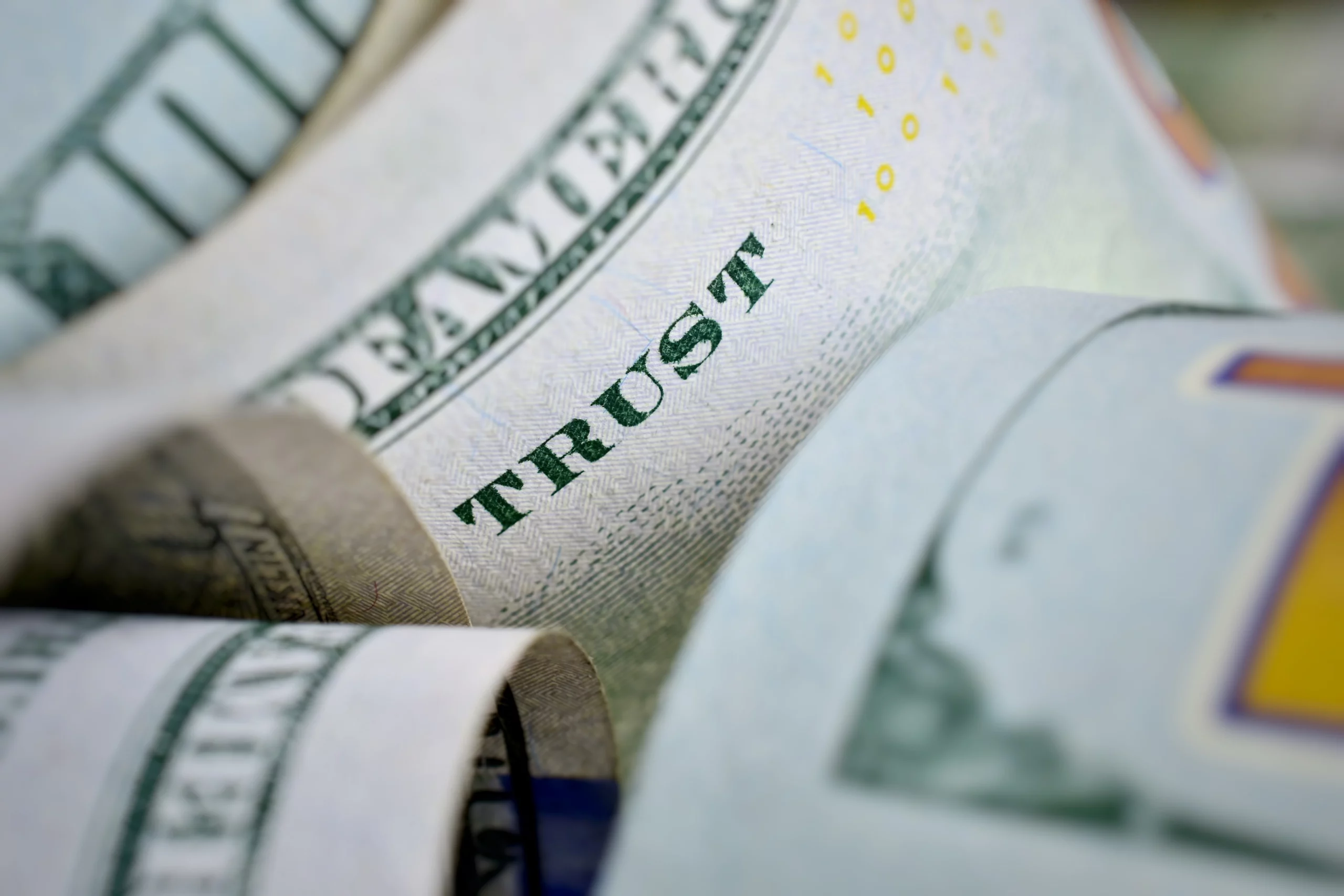 Close-up of a rolled US hundred-dollar bill showing the word ‘TRUST,’ symbolizing financial management, fiduciary responsibility, and reasonable trustee fees in California estate planning.